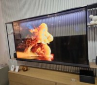 Le LG Signature Oled T de 77 pouces avec une toile noire derrière en train d'être rétractée // Source : Frandroid