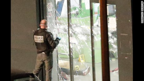 A police officer closes the bullet ridden door next to a body lying in a kosher market in Paris on Friday, January 9.