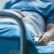 Sick patient lying in hospital bed, with a heart rate monitor on his finger