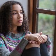 Sad teen girl with curly black hair looking out window