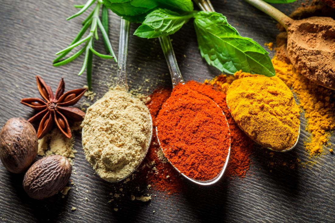 various herbs, spices, and seasoning on spoons, surrounded by star anise, and leaves.