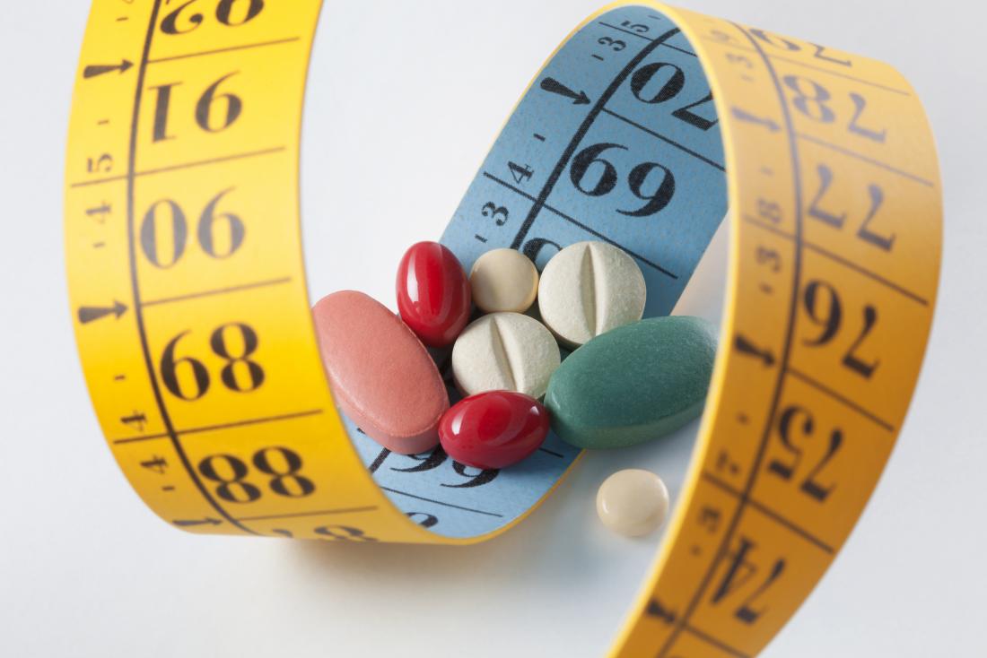 Weight loss and diet pills surrounded by measuring tape.