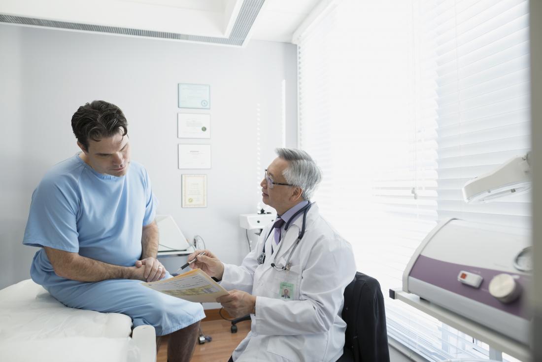 Man sitting on bed in gown in doctors office listening to an explanation.