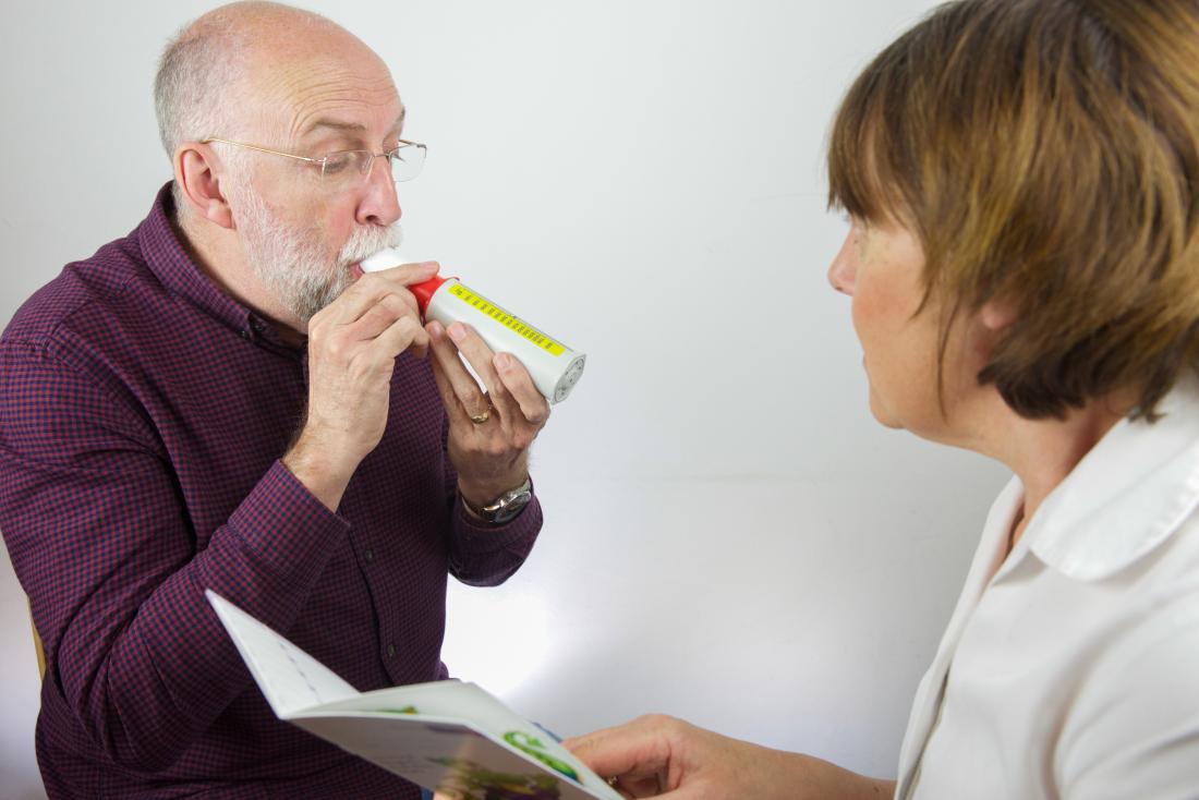 Man breathing into peak flow meter to test lung capacity as part of pulmonary function tests.