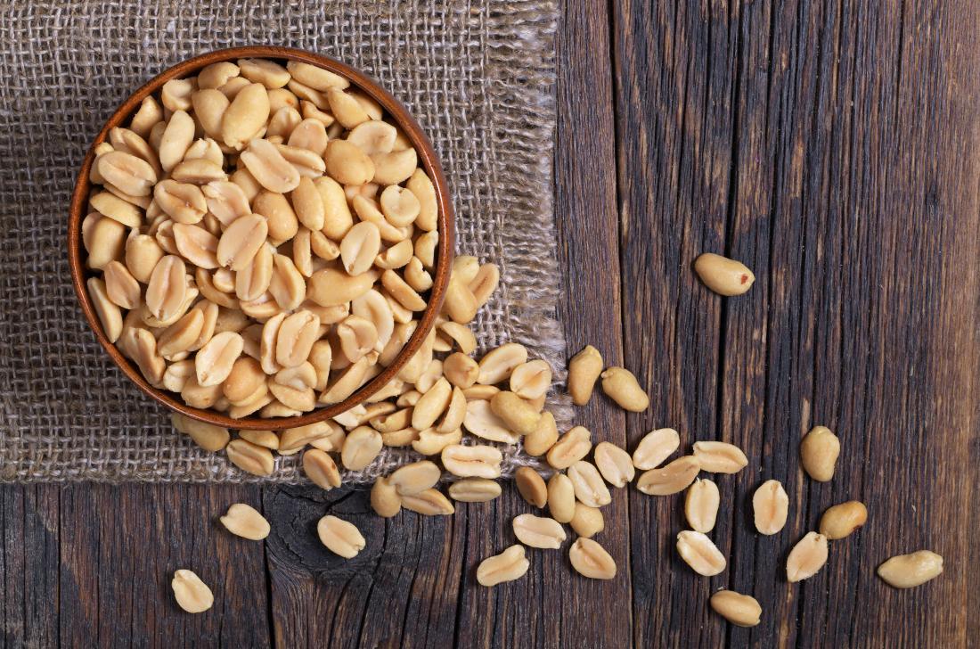 Peanuts in a bowl on wooden table top down view.