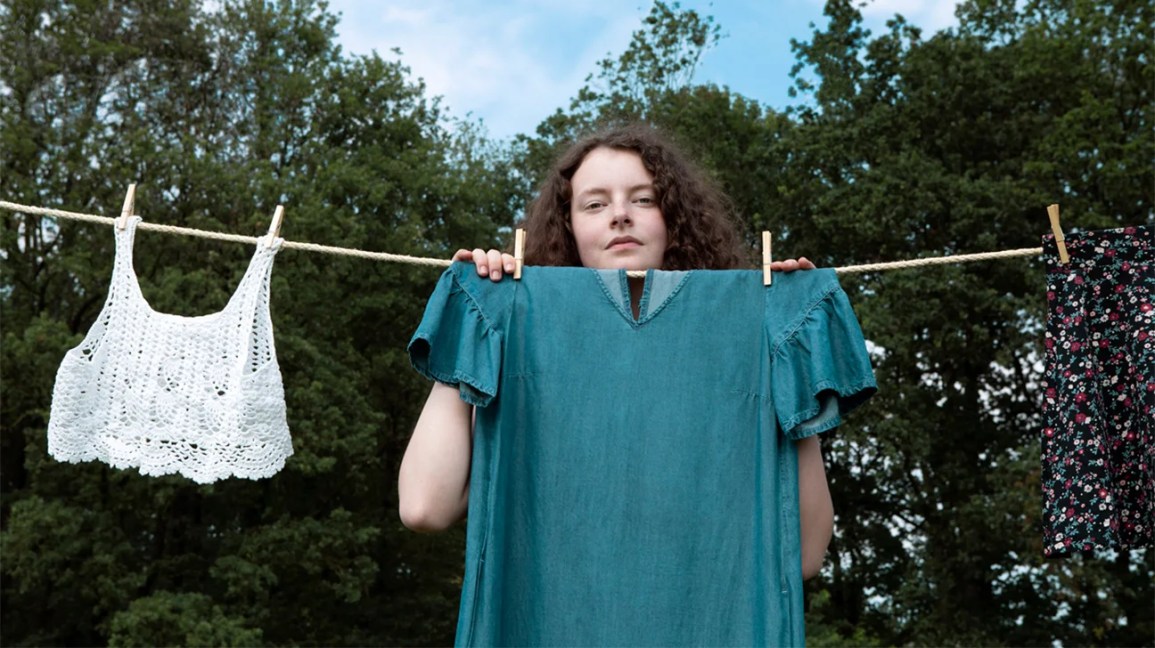 A woman with a negative body image hides behind clothing on a wash line. 