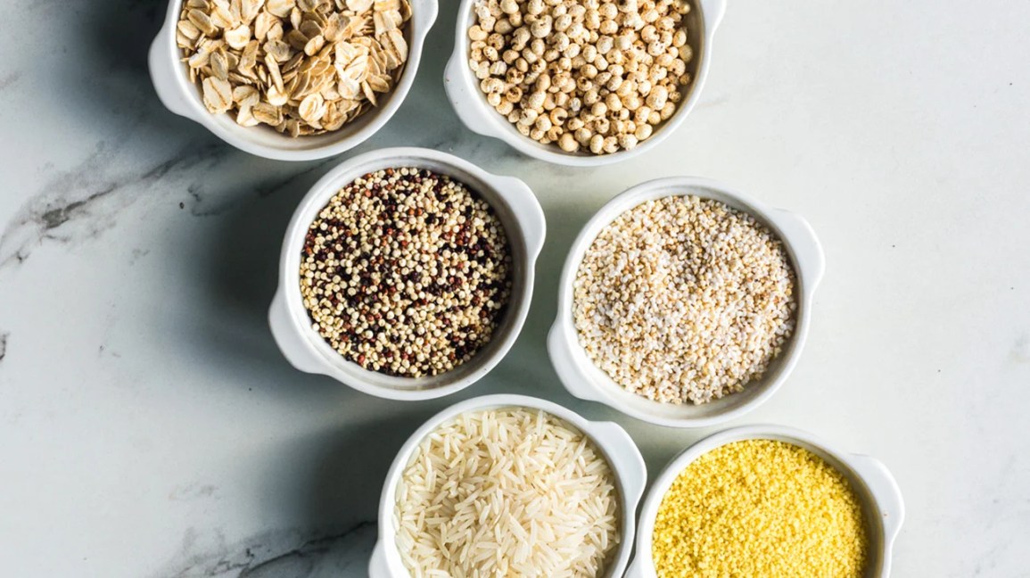 Various grains in small measuring cups on a counter.