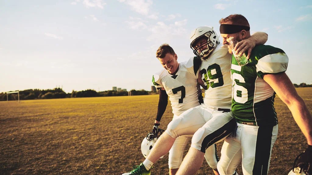 an injured football player with groin pain being carried off the pitch by two team members