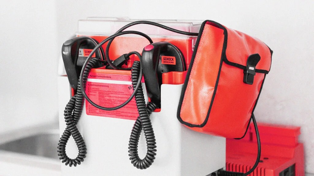A red and black defibrillator machine, which someone might use to help someone experiencing cardiac arrest.