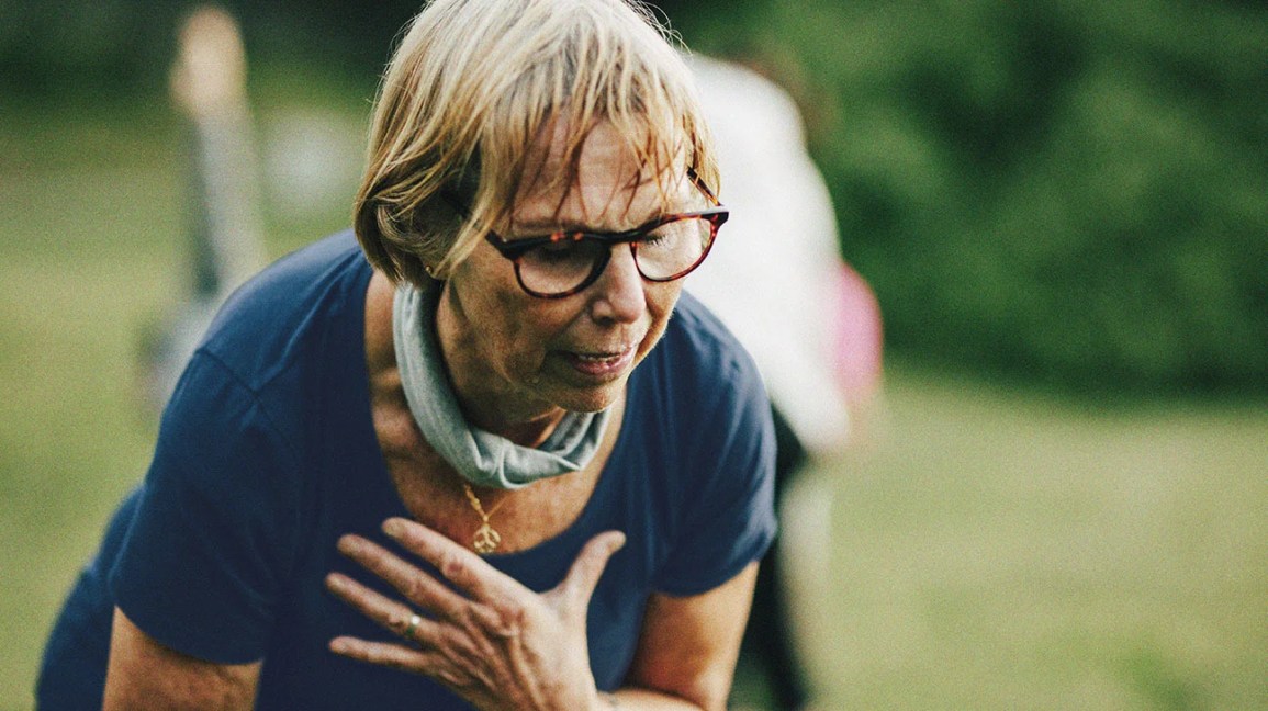 An older woman bending over and holding her chest due to angina, a symptom of heart disease in women.