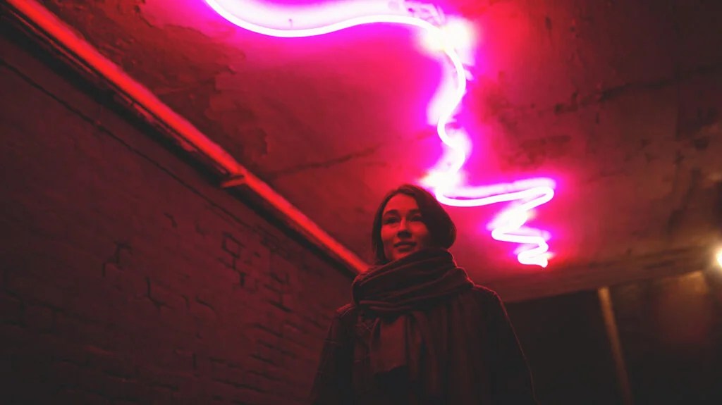 A woman walking through an underpass, with a red neon light zig-zagging above her, symoblizing the pain of a headache.