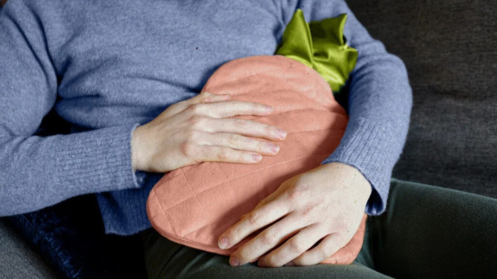 a person uses a hot water bottle to relieve symptoms of digestive problems