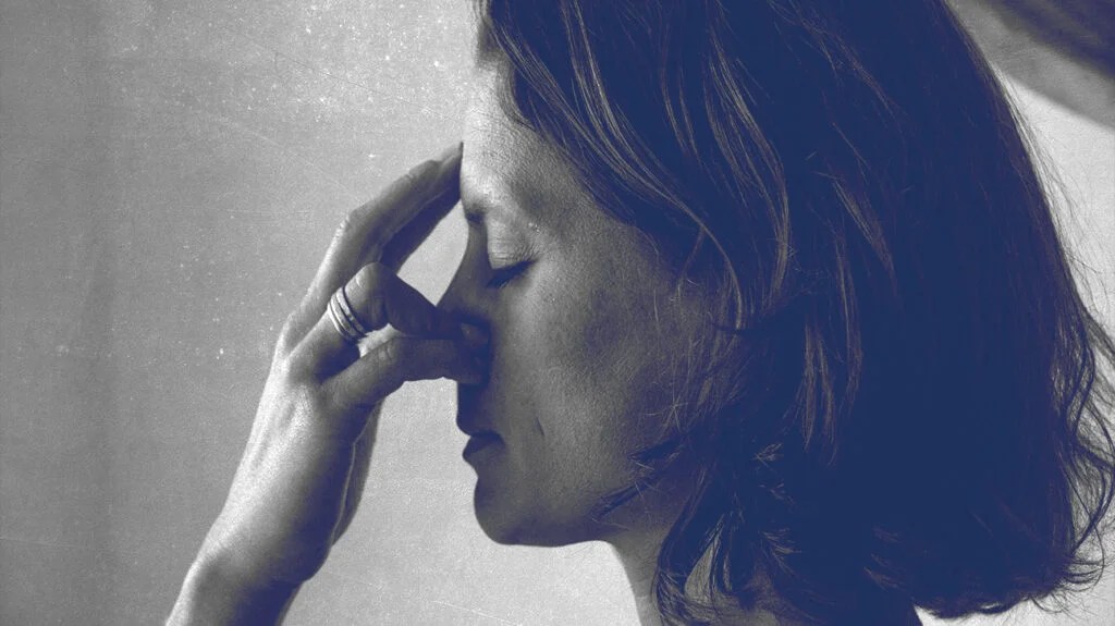 A woman facing left, holding her nose in pain due to a sinus headache.