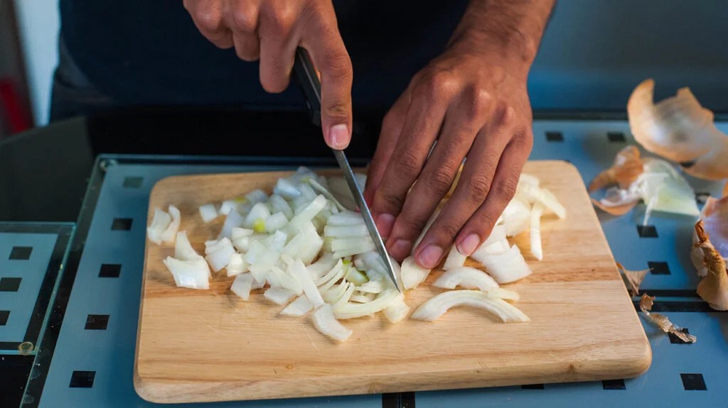 A person chopping onions on a wooden board for a heart healthy recipe.