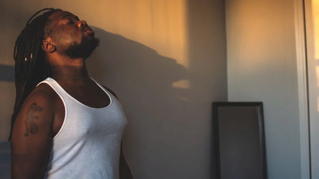 A man leaning with his back to the wall, inhaling deeply.