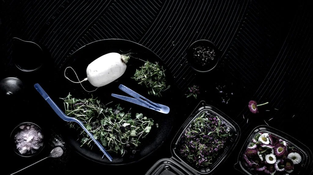 Salad ingredients, including various greens and daikon, in bowls on a table