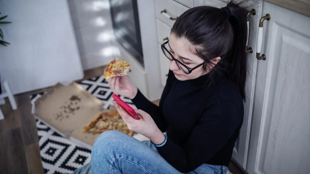 Person sat on a kitchen floor eating pizza