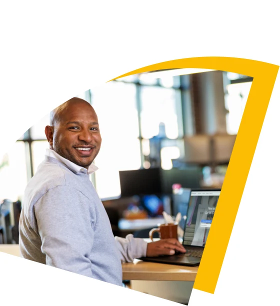 A man sitting at his work desk with his laptop and smiling towards the camera