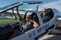 With the canopy of their glider raised, female cadets in sunglasses laugh in the two-seater cockpit of an Air Force Academy glider.