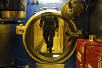 A crew member walks up to a water-tight hatch in the narrow passageway of the submarine U.S.S. Alaska