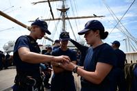 Cadets in T-shirts and ball are pictured in an activity with a sailing ship's masts in the background.