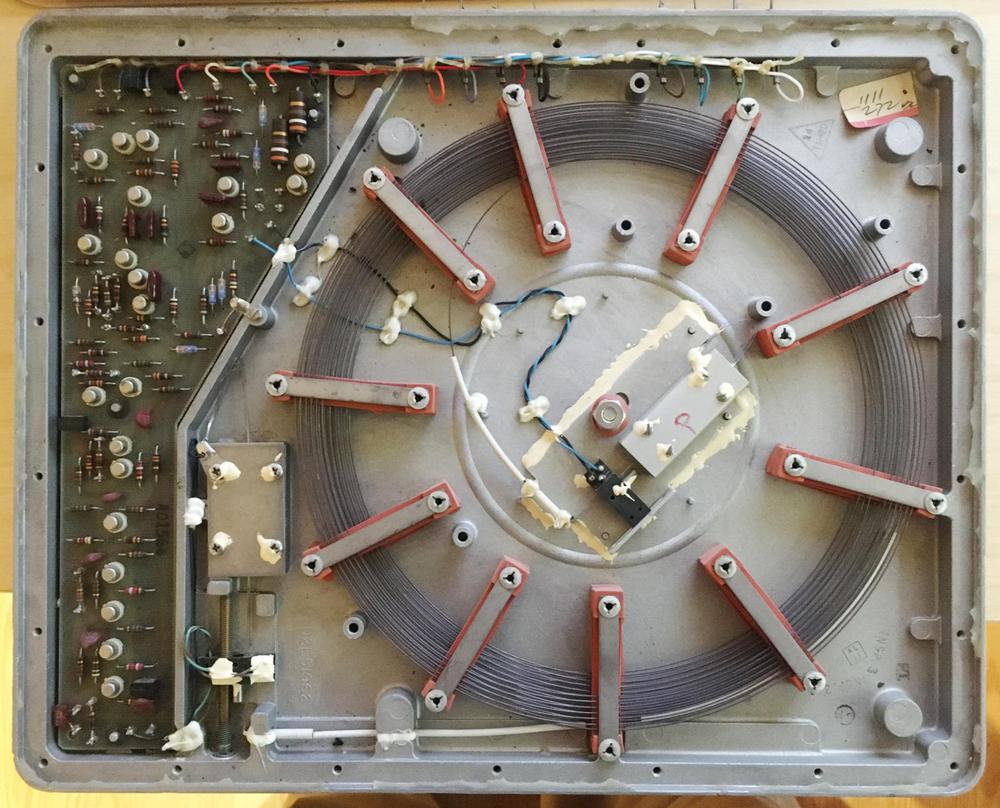 The coiled nickel wire inside a sonic delay has transducers at both ends (center and bottom left, with twisted wiring attached).
To adjust the delay, the threaded rod (bottom left) moves the transducer's position along the wire. The metal boxes on the ends of the wires are
dampers to prevent reflections. Photo courtesy of Alan Parker.