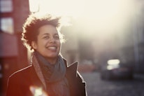 Happy urban women in her 30s walking outside on a chilly day with the sun behind her