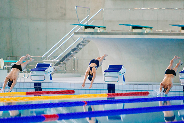 Two male swimmers and one female swimmer in diving position