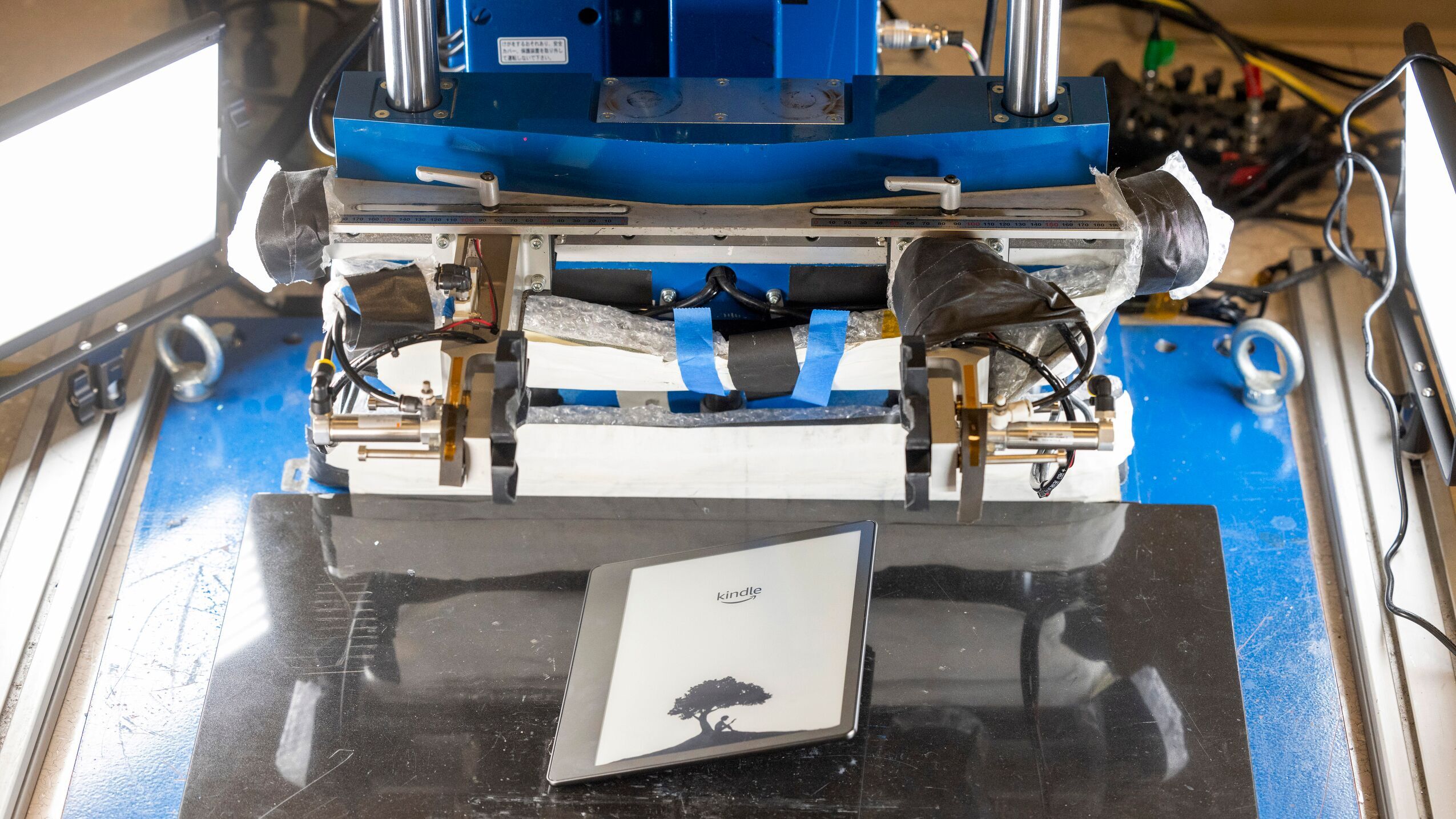 An image of a machine with two claw-like arms dropping a Kindle device onto a platform below it.