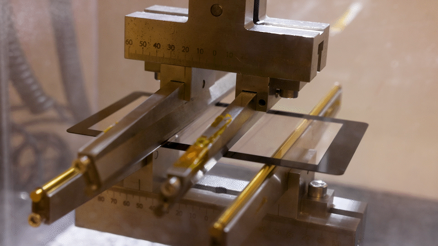 An animated GIF showing a piece of Kindle glass being held in place while a machine puts pressure on the glass until it bursts.