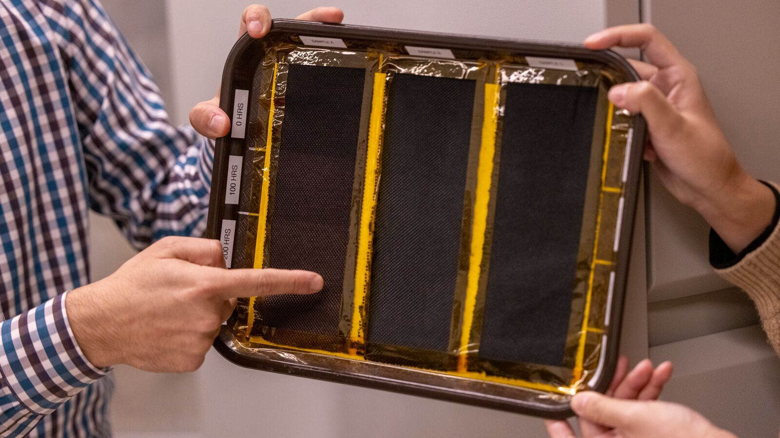 An image of a tray holding three strips of black fabric. Some of the strips are slightly more faded than others. 