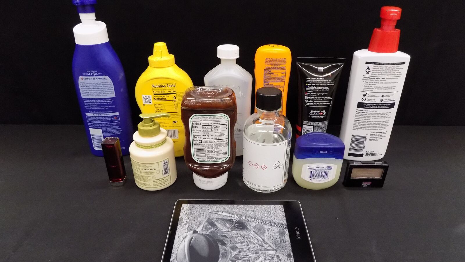 An image of various product bottles lined up behind a Kindle device. The products include things like sunscreen, ketchup, lotion, and lip balm.