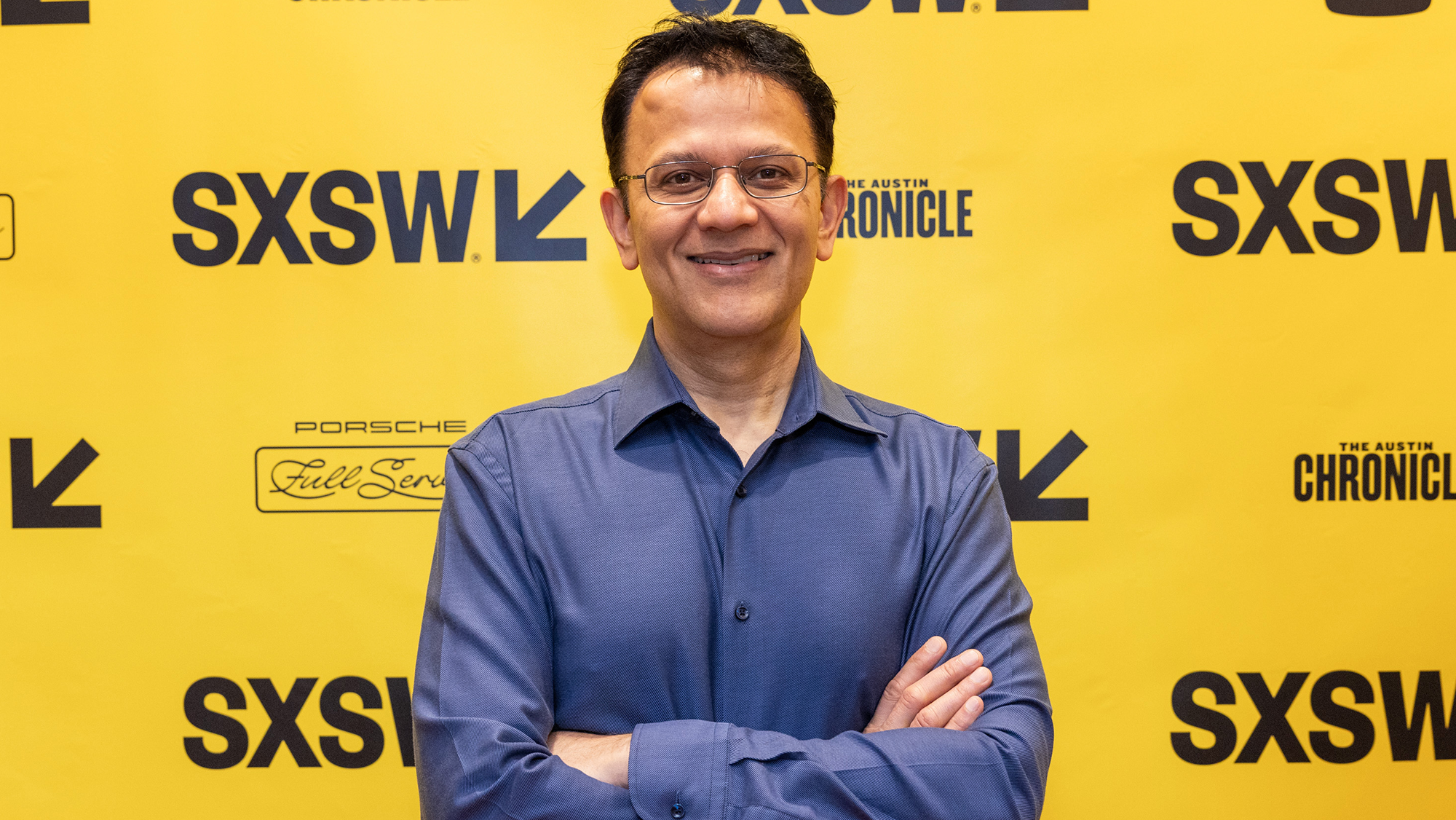 A photo of Vishal Sharma, Vice President, Artificial General Intelligence, standing with his arms crossed in front of a SXSW 2024 backdrop.