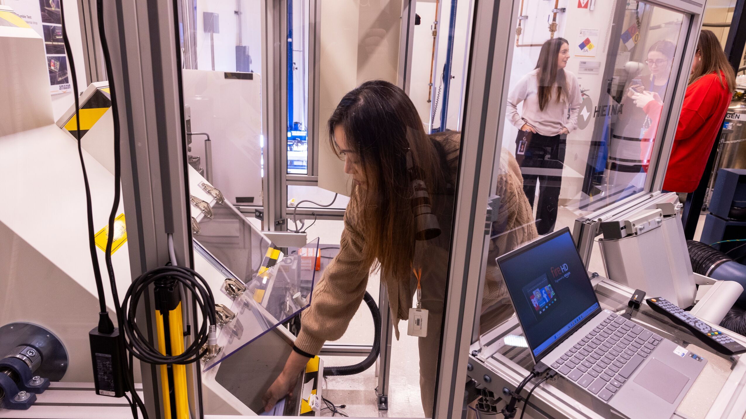 An image of a woman inside Amazon's Lab126, where they test various device prototypes. She is opening the door on a large machine and reaching in to grab something. 