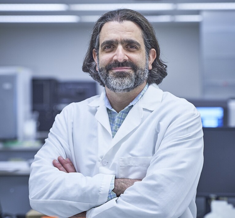 Adam Resnick wears a white doctor's jacket and stands with his arms crossed in a lab.