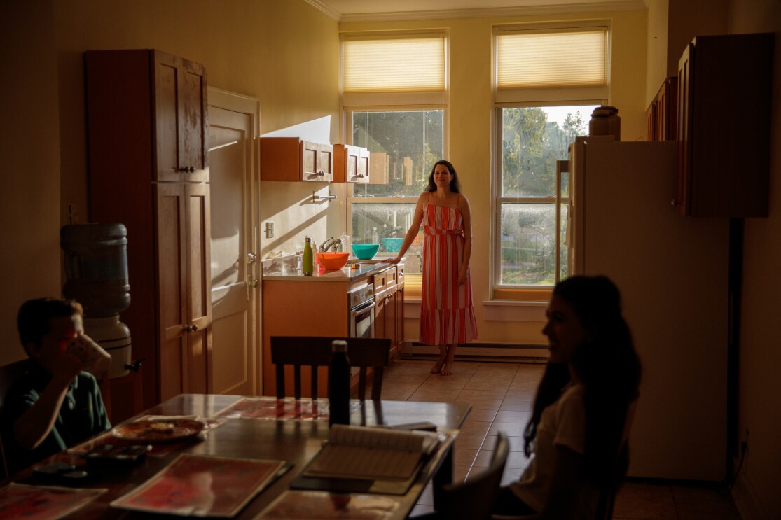 A woman stands in a sunlit kitchen.