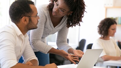 A photo of two students conversing in front of a laptop device. 