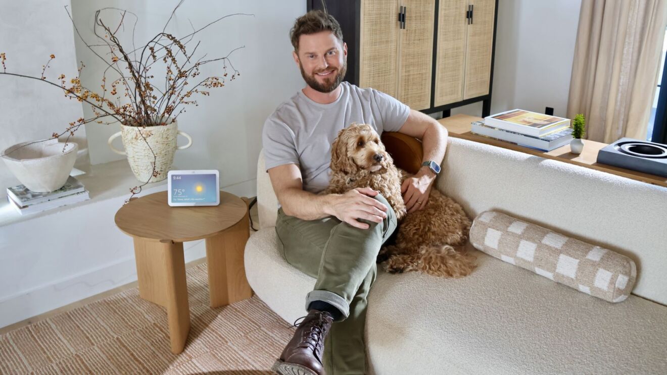 Bobby Berk sitting in a living room with a dog, decorative branches, and an Amazon Echo device