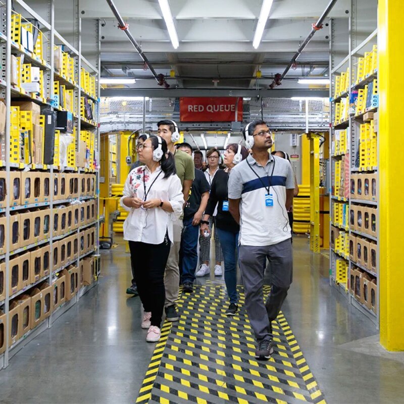 Group of people wearing headphones and walking down an aisle during an Amazon fulfillment center tour. 