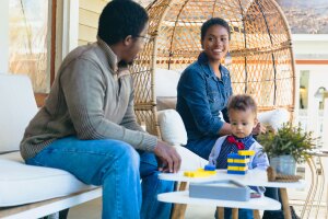 A photo of a couple sitting on a porch with their baby.