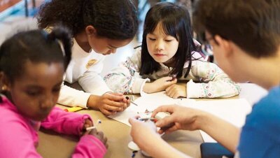 An image of four students interacting with miscellaneous objects at school.