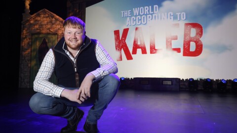 Kaleb Cooper squats on stage in front of his tour poster 