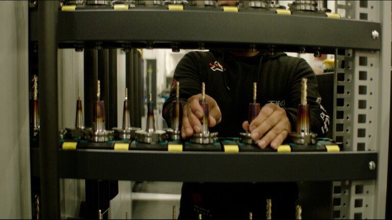 Person adjusting components in a complex mechanical setup with multiple precision tools visible.