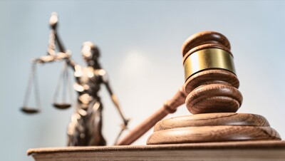 A gavel in the forefront and a statue holding a scale in the background. 