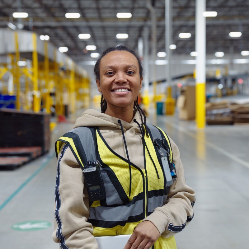 Image of employee Jessica standing in a fulfillment center holding her laptop and smiling.