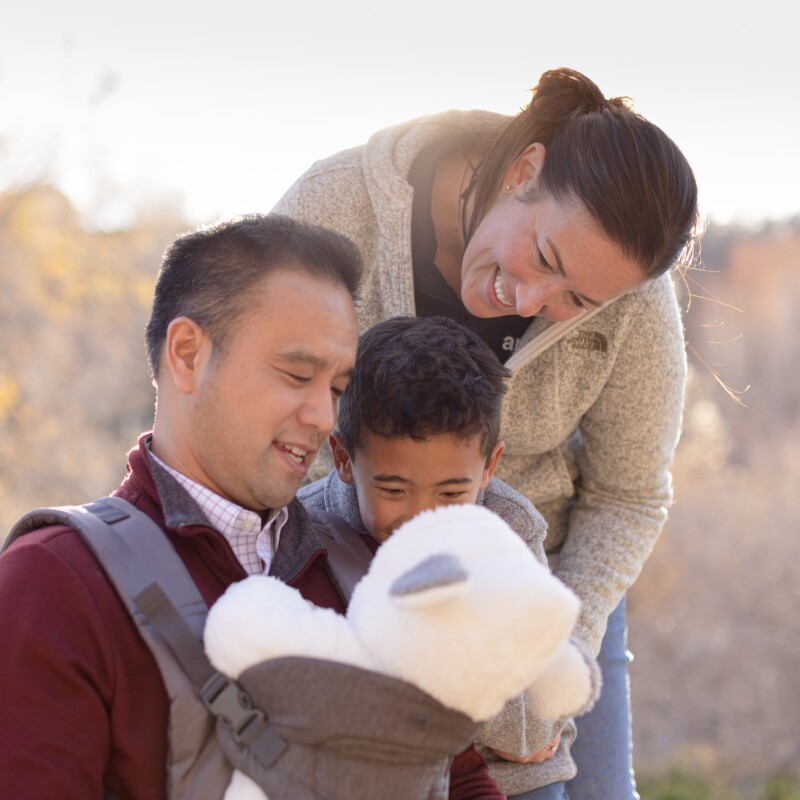 A man, woman, and child all look at an infant in a baby carrier.