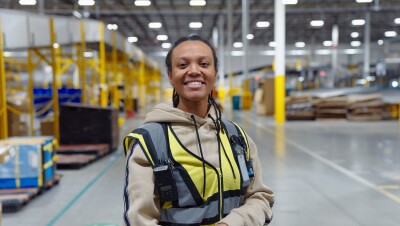 Image of employee Jessica standing in a fulfillment center holding her laptop and smiling.