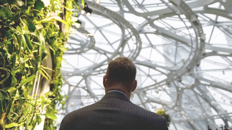 An image of the back of a man in a suit walking inside The Seattle Spheres at Amazon’s headquarters.
