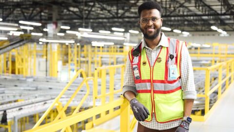 An image of Abdiaziz, an area manager working in an Amazon fulfillment center, wearing a yellow safety vest and gloves.