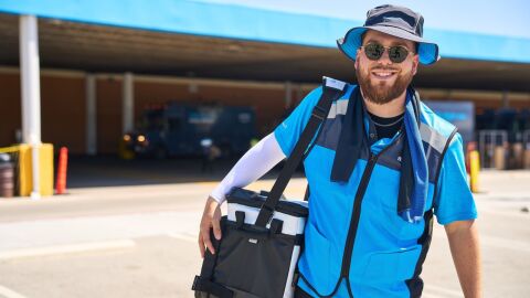 An image of an Amazon delivery driver wearing a bucket hat and carrying a cooler.